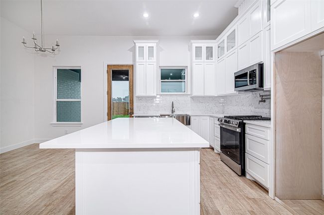 Kitchen with stainless steel appliances, light wood-type flooring, a center island, backsplash, and light countertops | Image 6