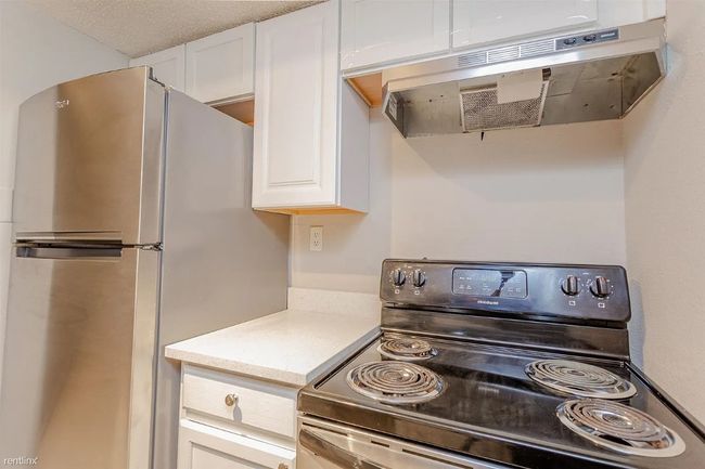 Kitchen featuring stainless steel appliances, under cabinet range hood, white cabinetry, and light countertops | Image 6