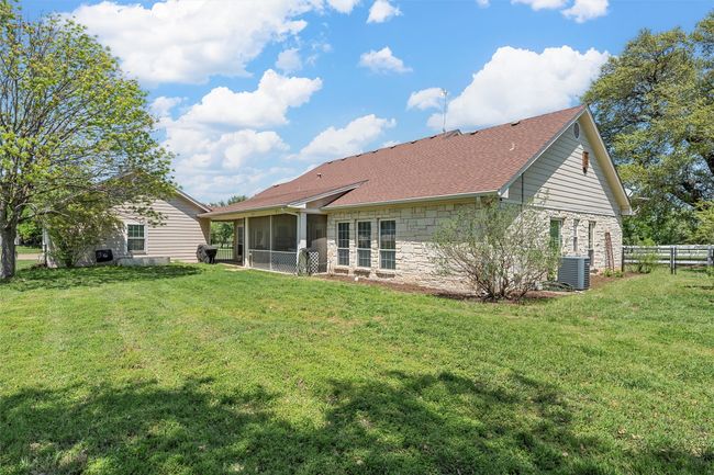 Rear view of property featuring cooling unit, stone siding, a sunroom, fence, and a lawn | Image 26