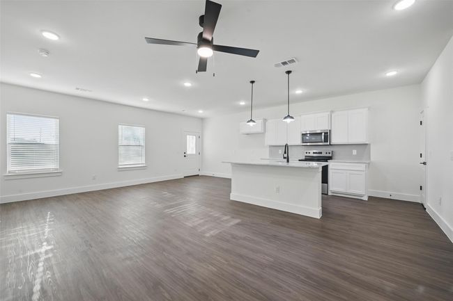 Kitchen with a ceiling fan, white cabinetry, appliances with stainless steel finishes, a center island with sink, and dark wood-style flooring | Image 7