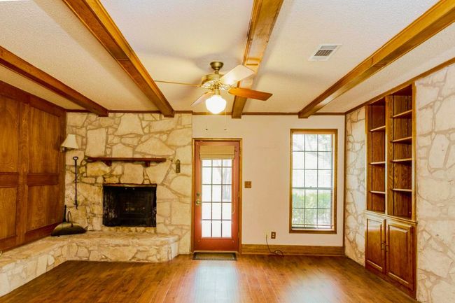 Unfurnished living room featuring beamed ceiling, wood finished floors, a fireplace, ceiling fan, and built in shelves | Image 5
