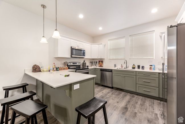 Kitchen with a kitchen breakfast bar, a peninsula, white cabinetry, appliances with stainless steel finishes, and a sink | Image 7