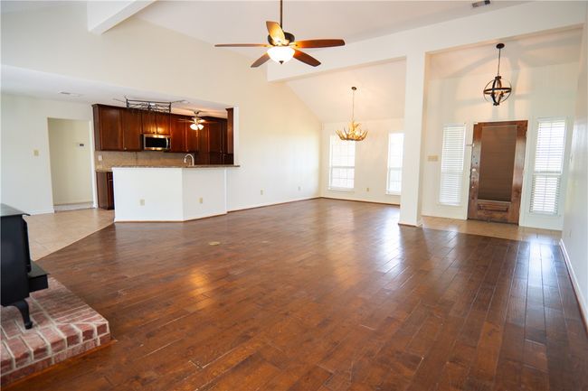 Unfurnished living room featuring ceiling fan, a chandelier, dark wood-type flooring, beam ceiling, and high vaulted ceiling | Image 22