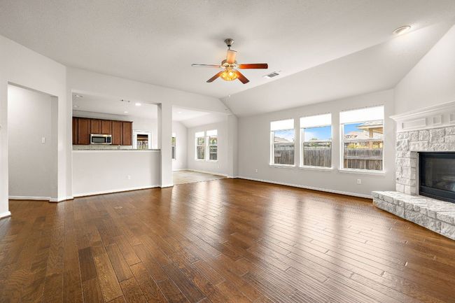 Unfurnished living room with lofted ceiling, visible vents, a ceiling fan, dark wood-type flooring, and a fireplace | Image 4