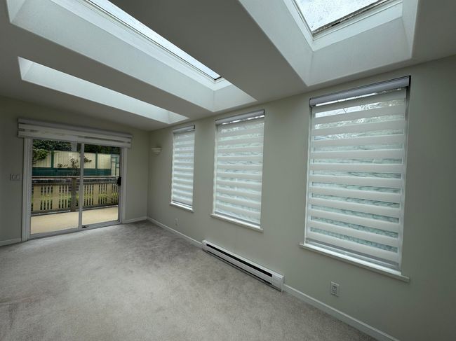 Empty room with a skylight, carpet flooring, baseboards, and a baseboard heating unit | Image 11
