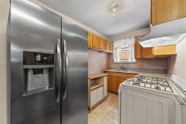 Kitchen featuring stainless steel refrigerator with ice dispenser, white gas range, backsplash, light tile patterned flooring, and ventilation hood | Image 25