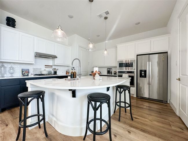 Kitchen with appliances with stainless steel finishes, range hood, decorative backsplash, a kitchen breakfast bar, and white cabinets | Image 9