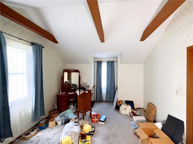 Carpeted bedroom with multiple windows, lofted ceiling, wallpapered walls, and an office area | Image 12