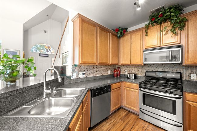 Kitchen with appliances with stainless steel finishes, a dual sink, tasteful backsplash, and dark countertops | Image 11