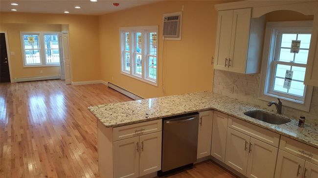 Kitchen with stainless steel dishwasher, a baseboard radiator, decorative backsplash, and light stone counters | Image 6