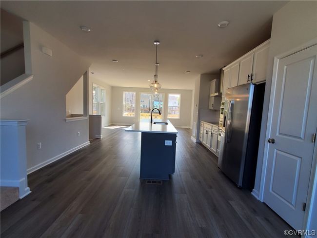 Kitchen featuring dark hardwood floors, a wealth of natural light, hanging light fixtures, backsplash, black electric stovetop, and stainless steel fridge | Image 20