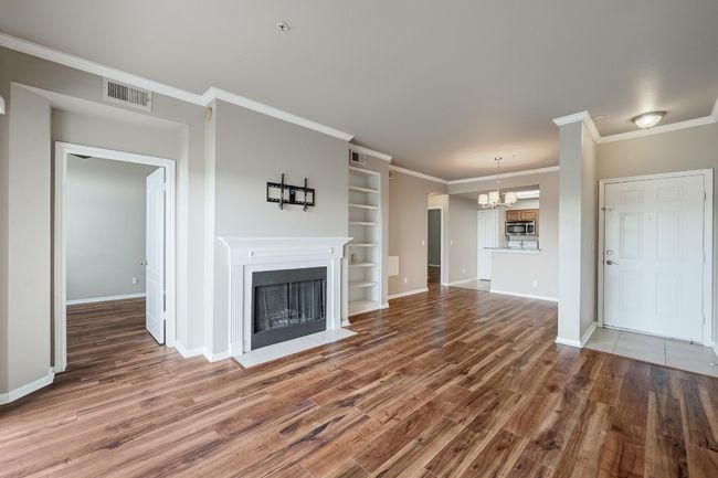 Unfurnished living room with wood finished floors, a chandelier, a fireplace with flush hearth, ornamental molding, and built in features | Image 11