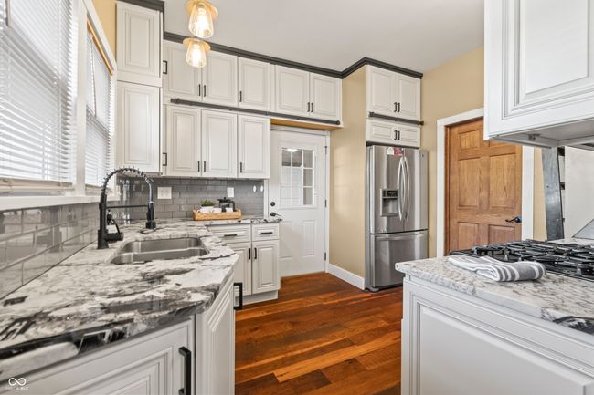kitchen with light stone countertops, stainless steel fridge with ice dispenser, dark wood-type flooring, white cabinets, and backsplash | Image 17