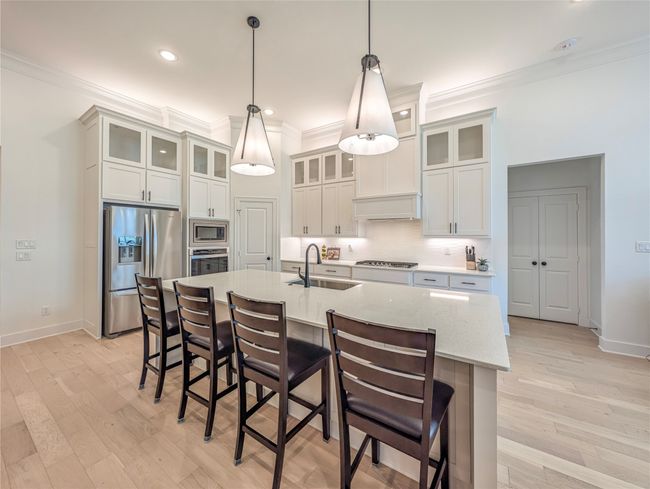 Kitchen with stainless steel appliances, ornamental molding, a kitchen breakfast bar, an island with sink, and light wood-style flooring | Image 6