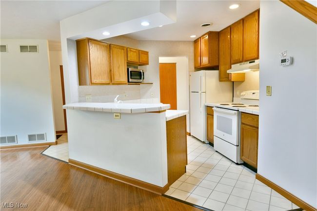 Kitchen featuring white appliances, under cabinet range hood, tile counters, a peninsula, and recessed lighting | Image 8