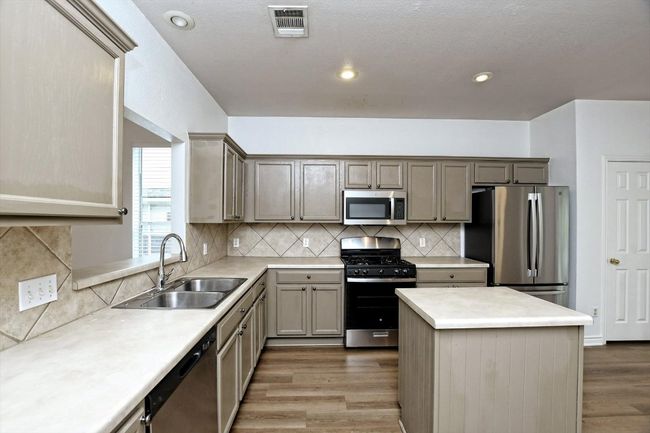Kitchen with appliances with stainless steel finishes, wood finished floors, light countertops, a center island, and tasteful backsplash | Image 6