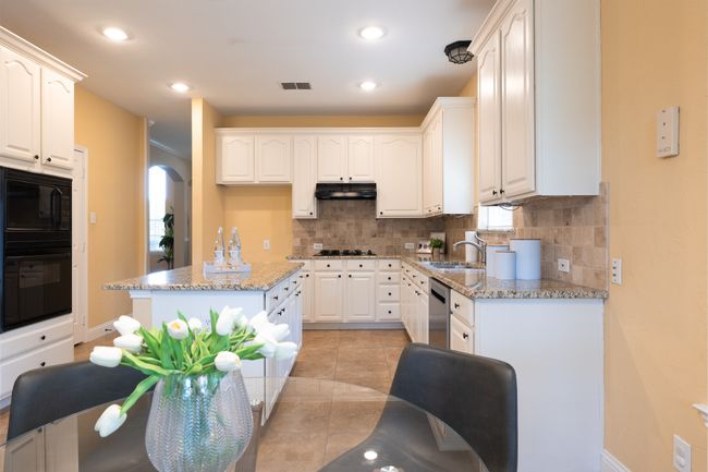 Kitchen featuring black appliances, under cabinet range hood, decorative backsplash, light stone counters, and white cabinets | Image 14