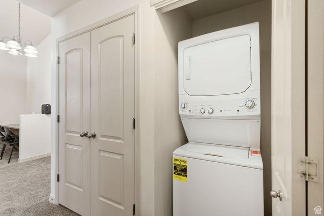 Laundry area with stacked washer and clothes dryer, carpet flooring, and a chandelier | Image 18