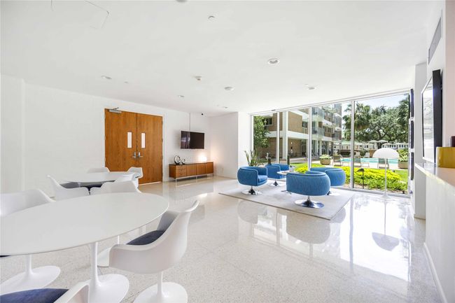 This bright, modern lounge features sleek white flooring and contemporary furniture, with large windows offering a view of a lush garden and pool area, creating a serene and inviting atmosphere. | Image 25