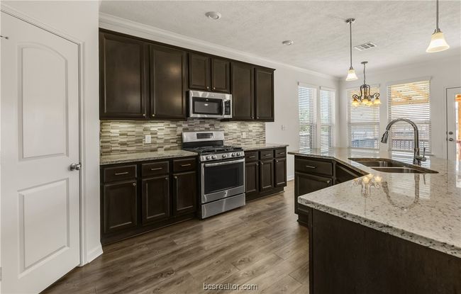 Kitchen featuring pendant lighting, sink, dark brown cabinets, stainless steel appliances, and decorative backsplash | Image 7