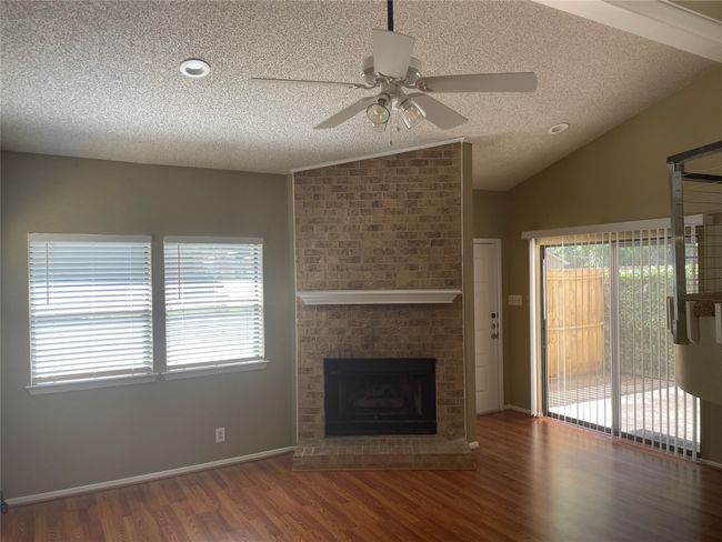 Unfurnished living room featuring lofted ceiling, ceiling fan, a brick fireplace, a textured ceiling, and dark hardwood / wood-style flooring | Image 13