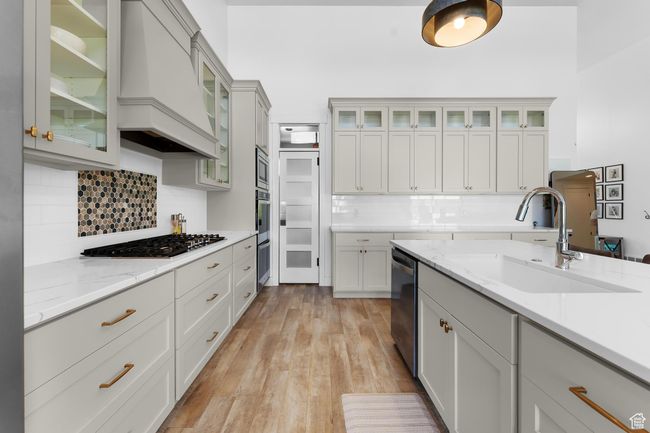 Kitchen featuring appliances with stainless steel finishes, custom exhaust hood, decorative backsplash, light wood-type flooring, and light stone countertops | Image 8