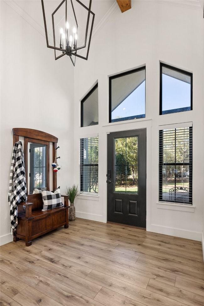 Foyer with crown molding, healthy amount of natural light, a towering ceiling, light wood finished floors, and a chandelier | Image 32