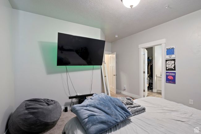 Bedroom with baseboards, light colored carpet, a spacious closet, a textured ceiling, and a closet | Image 9