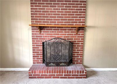 Interior details featuring a brick fireplace, wooden walls, and carpet flooring | Image 3