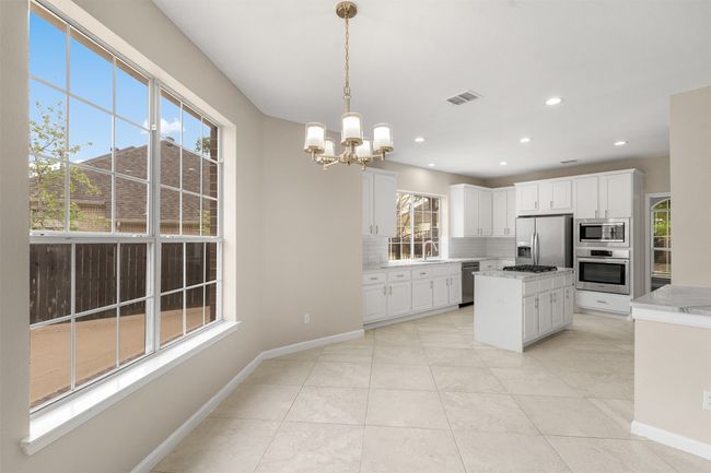Kitchen featuring white cabinetry, an inviting chandelier, stainless steel appliances, decorative backsplash, and visible vents | Image 16