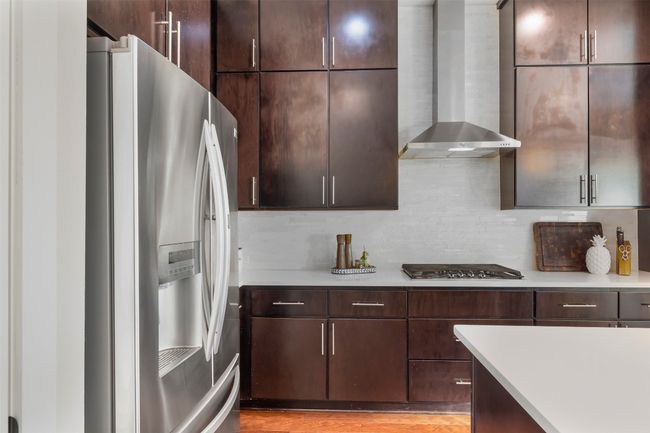 Kitchen with stainless steel appliances, wall chimney exhaust hood, light countertops, backsplash, and dark brown cabinets | Image 29