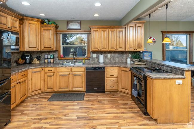 Kitchen featuring sink, light hardwood / wood-style flooring, hanging light fixtures, kitchen peninsula, and black appliances | Image 13