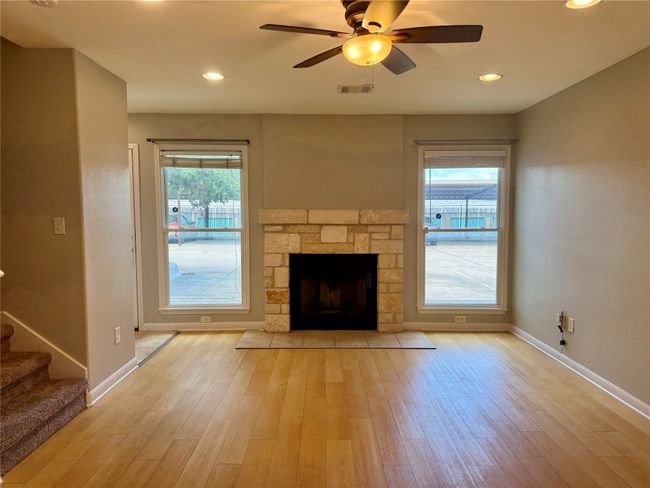 Unfurnished living room featuring ceiling fan, light wood finished floors, a fireplace, stairway, and recessed lighting | Image 4