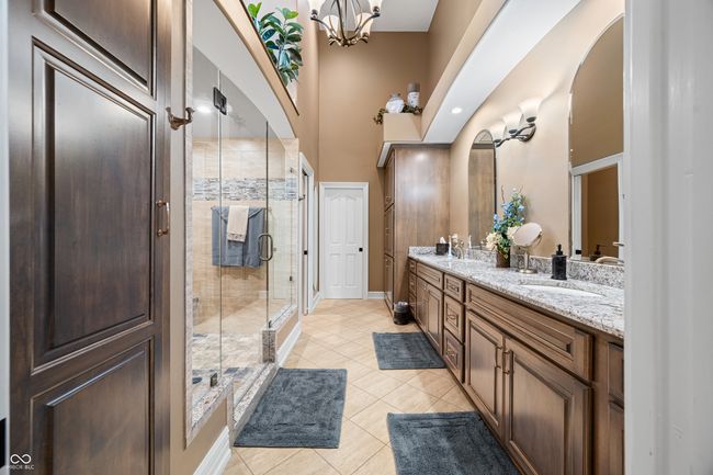 bathroom with a shower stall, double vanity, baseboards, a notable chandelier, and tile patterned flooring | Image 48