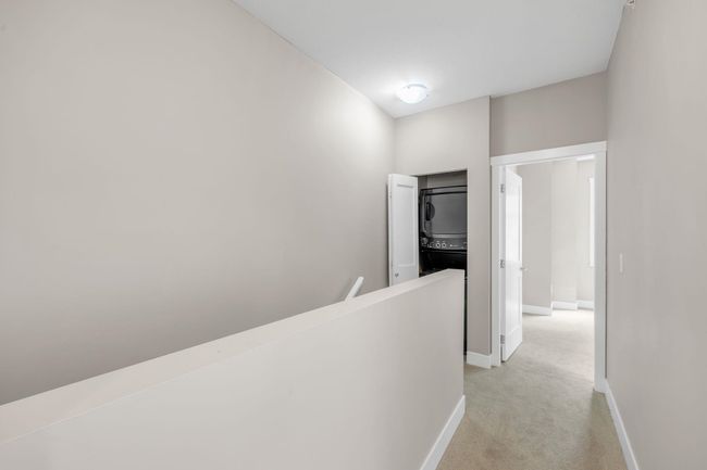 Corridor featuring stacked washer and clothes dryer, an upstairs landing, and light carpet | Image 16