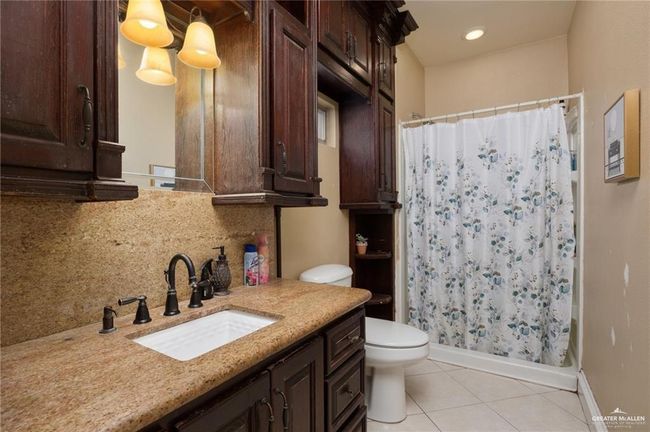 Full bathroom featuring backsplash, tile patterned floors, vanity, shower / tub combo with curtain, and toilet | Image 9