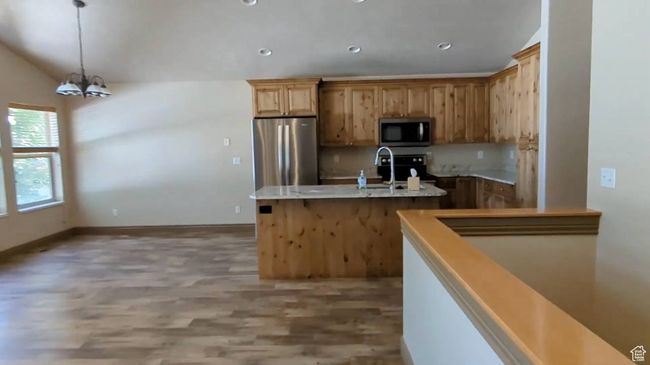 Kitchen featuring appliances with stainless steel finishes, a sink, light wood-style flooring, an island with sink, and a chandelier | Image 14