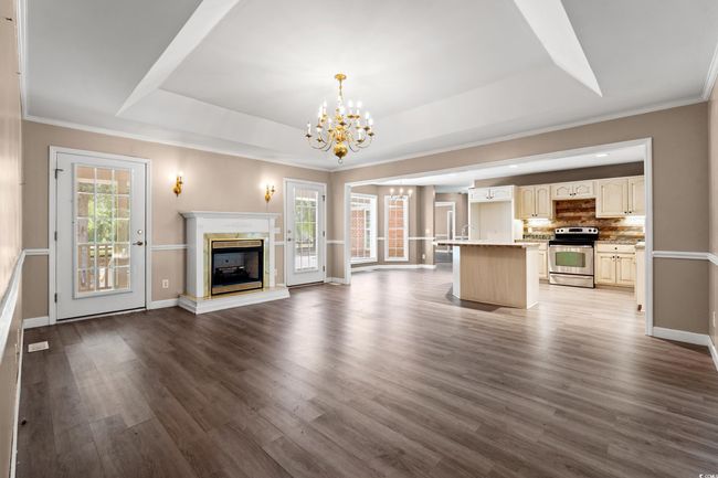 Unfurnished living room featuring a raised ceiling, a chandelier, dark wood-type flooring, a premium fireplace, and crown molding | Image 13
