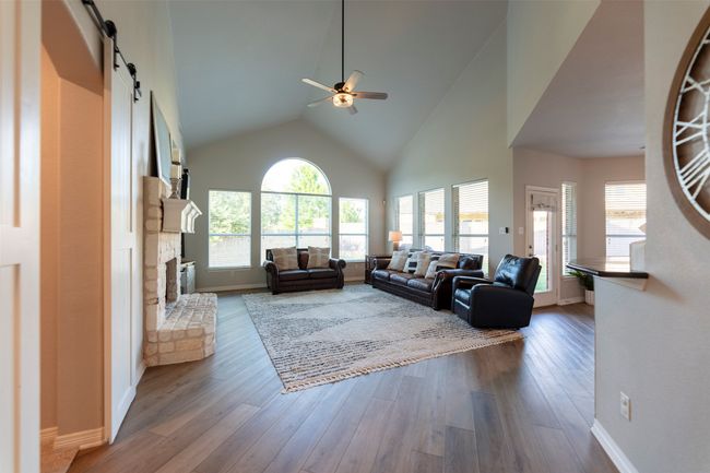 Living area featuring a ceiling fan, a barn door, a fireplace, wood finished floors, and high vaulted ceiling | Image 11