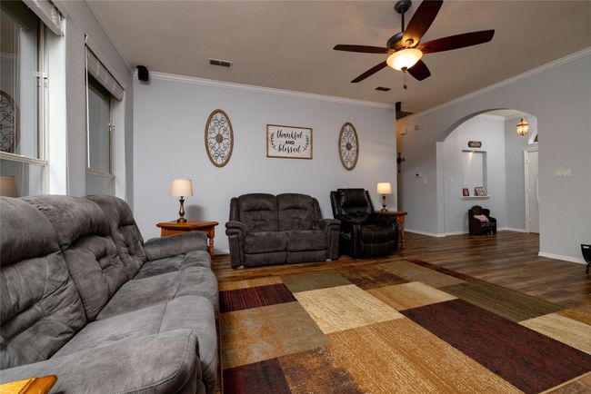 Living area featuring a ceiling fan, wood finished floors, arched walkways, ornamental molding, and visible vents | Image 11