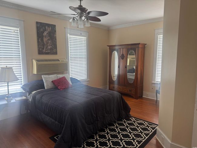 Bedroom featuring wood finished floors, crown molding, a wall mounted air conditioner, and ceiling fan | Image 17