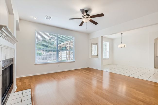 Unfurnished living room with a tiled fireplace, light wood-style floors, a ceiling fan, baseboards, and a chandelier | Image 16