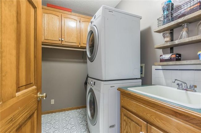 Laundry room featuring baseboards, a sink, stacked washer / dryer, and cabinet space | Image 43