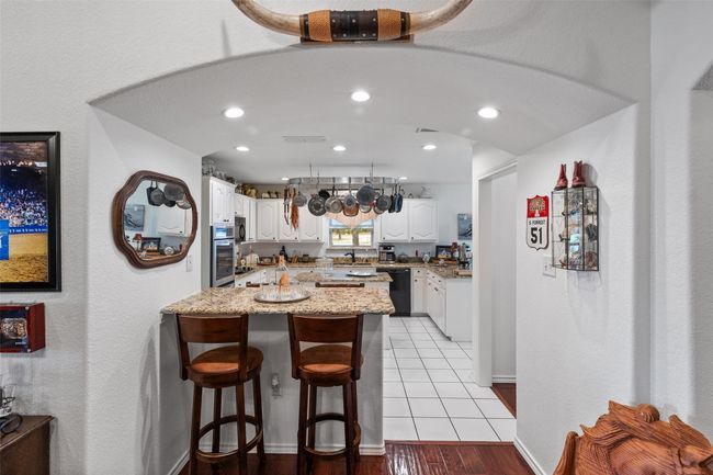 Kitchen with a sink, light stone counters, white cabinetry, a kitchen bar, and black appliances | Image 7