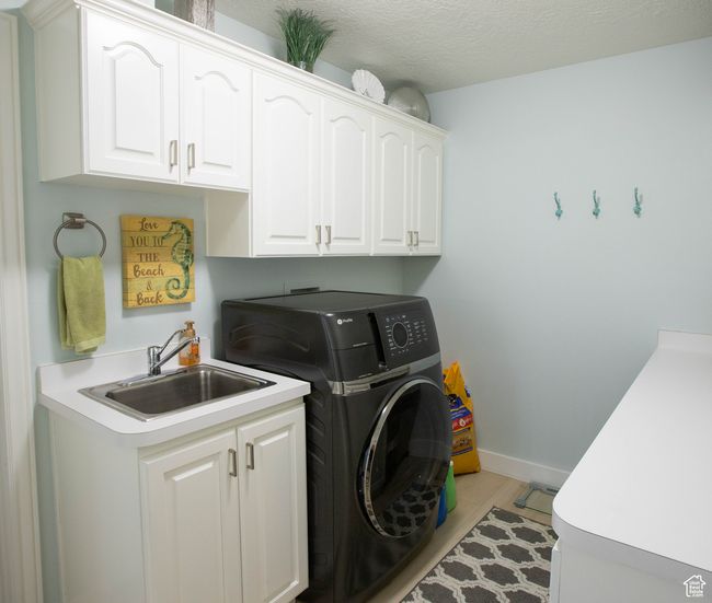 Laundry area featuring cabinet space, washer / dryer, light wood-style floors, and baseboards | Image 32