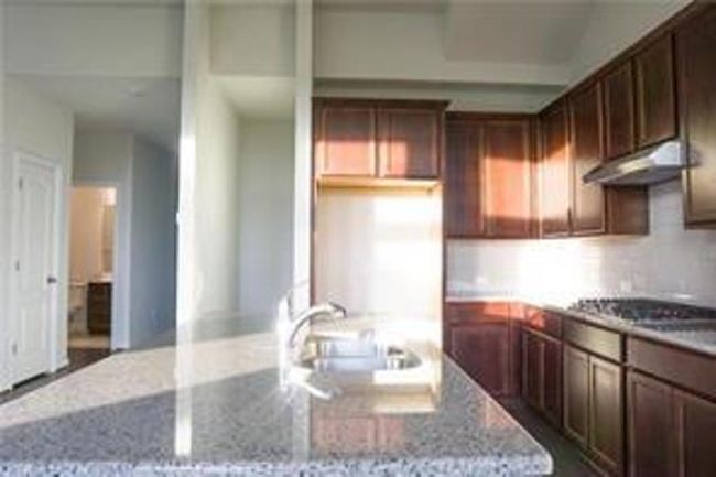 Kitchen featuring under cabinet range hood, light stone counters, an island with sink, and stovetop | Image 6