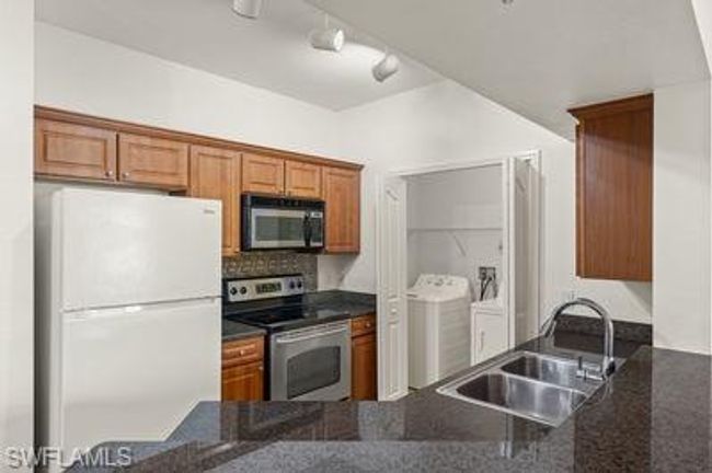 Kitchen with brown cabinetry, dark stone counters, stainless steel appliances, washer and dryer, and a sink | Image 16