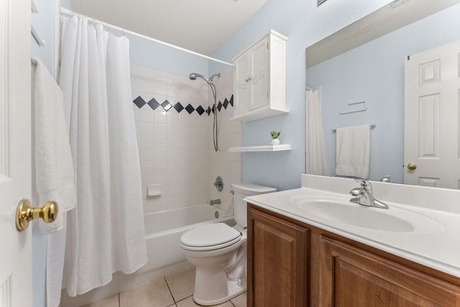 Full bathroom featuring toilet, tile patterned floors, shower / bath combo with shower curtain, and vanity | Image 23