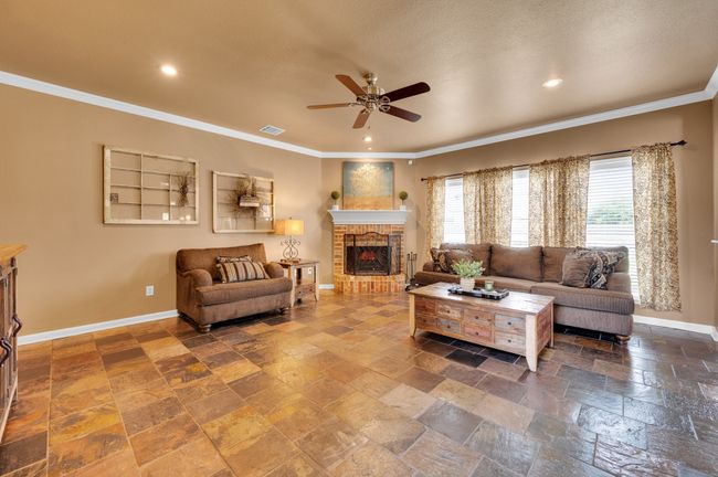 Living room featuring a ceiling fan, recessed lighting, stone tile flooring, crown molding, and a fireplace | Image 7