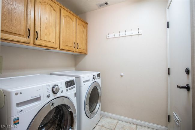 Clothes washing area with cabinet space, washing machine and clothes dryer, baseboards, visible vents, and light tile patterned flooring | Image 27